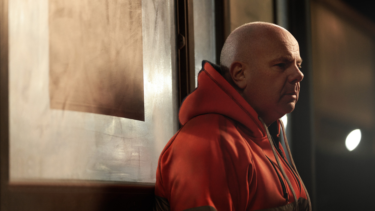 Still from Macmillan TV ad. Photo of a person in an orange, hooded jumper. Photo is their side profile as they look straight ahead.