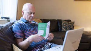 Steven sits on a sofa reading a cancer information leaflet. A laptop is open on his lap.