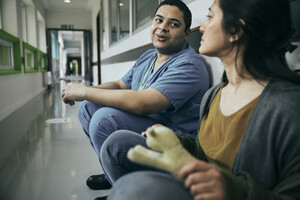 A Macmillan Professional supporting a person affected by cancer. They are sitting in a hospital corridor talking.