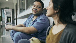 A Macmillan Professional supporting a person affected by cancer. They are sitting in a hospital corridor talking.