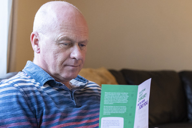 Steven sits on a sofa reading a cancer information leaflet. A laptop is open on his lap.