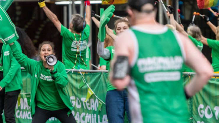 A Macmillan volunteer is cheering on a Macmillan runner with a megaphone as he runs past.