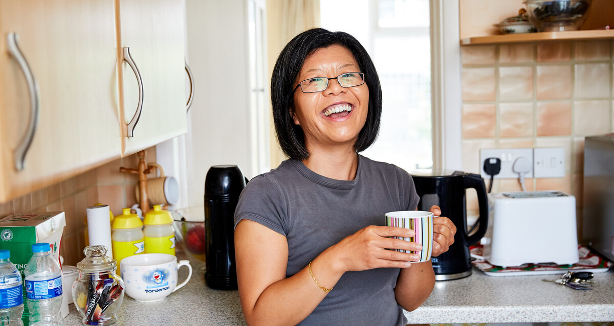 Woman at home in kitchen drinking coffee and smiling