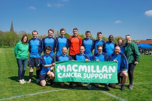 A football team wearing a blue kit and holding a Macmillan banner at the Manchester Grammar School Match 4 Macmillan