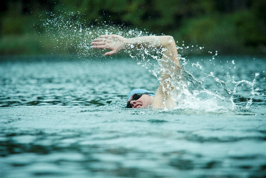 A man in a swim cap and goggles doing the front crawl in open water.