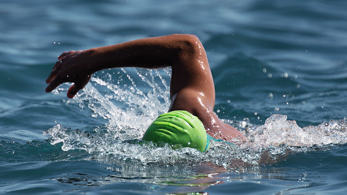A man swimming wearing a bright green swim cap does the front crawl in open water