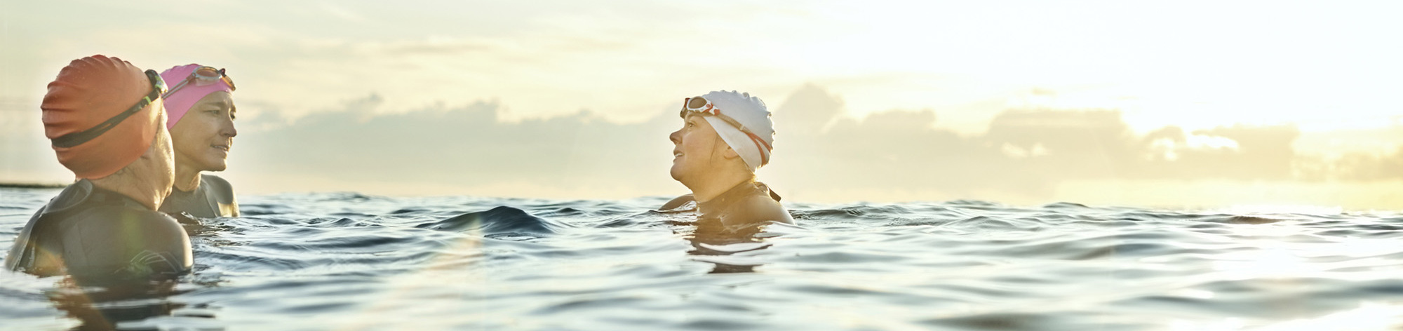 Three women in swim caps tread water together in open water