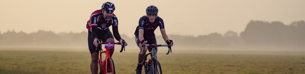 Two riders cycling down a country road. It is misty in the background.