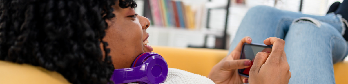 A woman lies on a couch playing a game on her mobile phone.