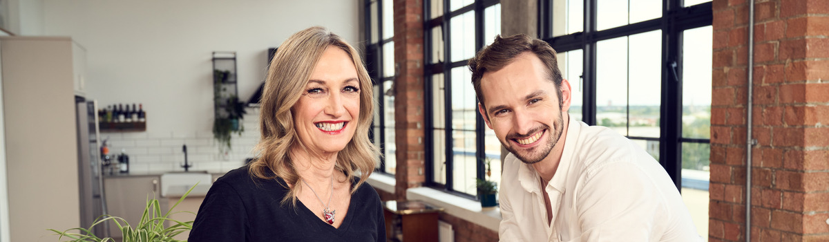 Macmillan storytellers Kathy and Adam are smiling and standing in front of La Roche Possay products in a modern kitchen.