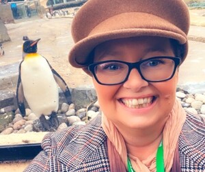 A lady wearing glasses, wearing a hat and a checked jacket.