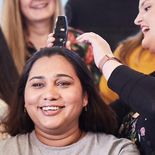 A woman preparing to have her hair shaved by someone holding electric clippers.