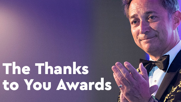 A man in a brocade dinner jacket and bow tie claps on stage, smiling at someone off camera. There is bold white text reading 'The Thanks to You Awards'