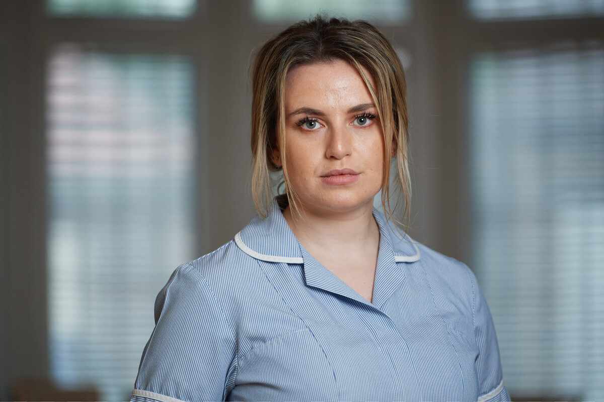 A lady healthcare professional with blonde hair wearing a blue dress.