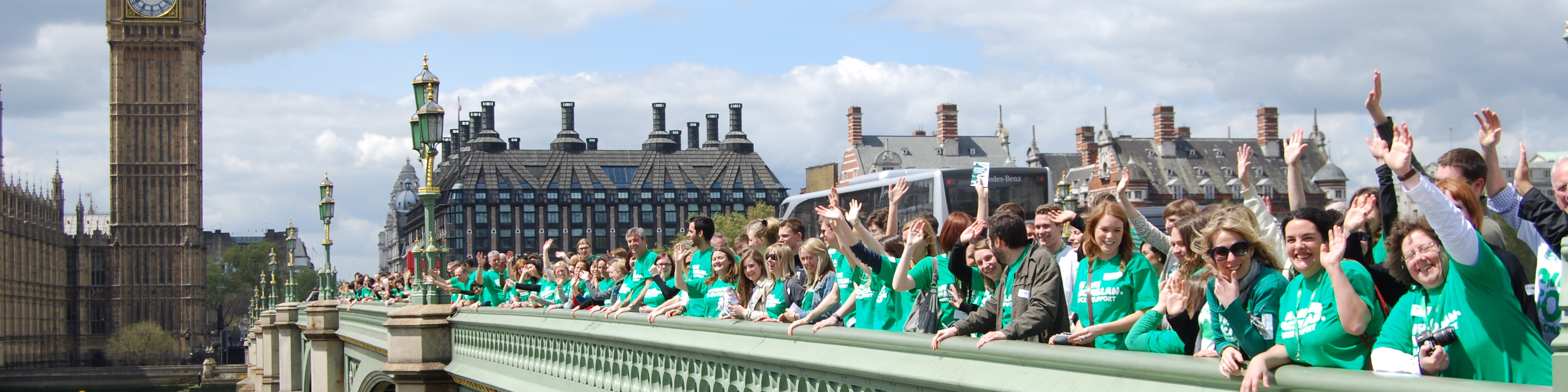 Macmillan staff gathered on Westminster Bridge outside the Houses of Parliament. They are wearing green Macmillan t-shirts. 