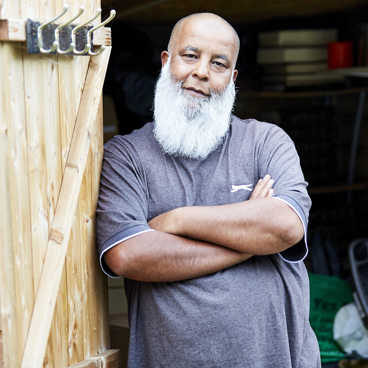 A middle-aged man with a beard and blue t-shirt stands outside a shed.