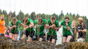 A group of people moving through coloured string and hay,